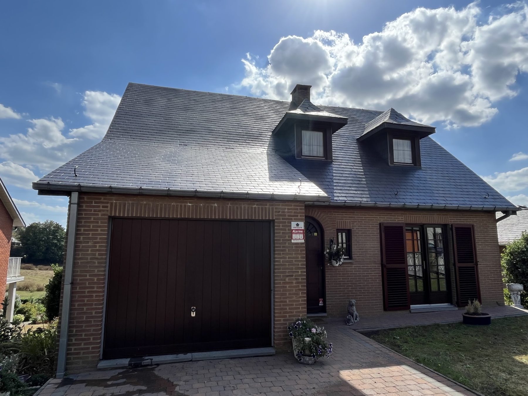 Maison au toit d'ardoise avec deux lucarnes, sous un ciel bleu